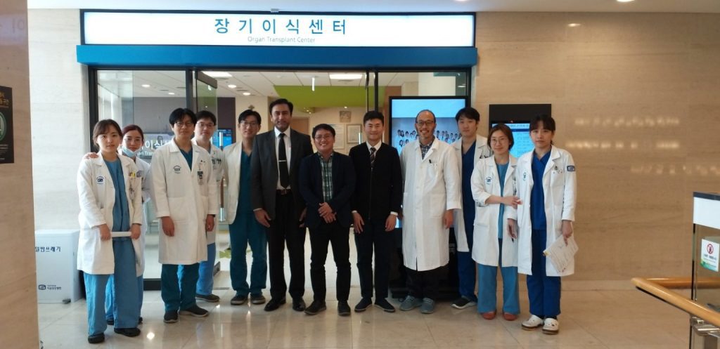 A group of doctors and medical staff, some in white coats and others in scrubs, stand together for a photo in front of a sign that reads "Organ Transplant Center" in both Korean and English.