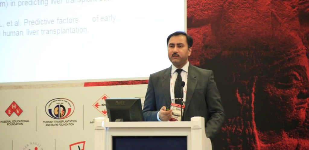 Dr. Muhammed Zakria stands at a podium giving a presentation. His name is displayed on the screen of the podium. A projection screen with medical text is visible behind him, along with logos of various medical foundations and organizations.